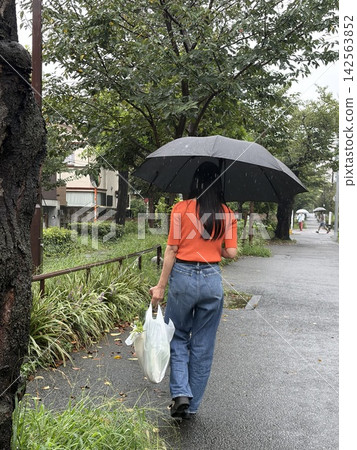 The back view of a woman walking with shopping bags on a rainy day. The back view of a woman walking with shopping bags on a rainy day. 142563852