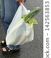 A woman carrying a shopping bag full of vegetables on a rainy day. 142563853