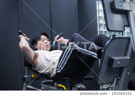 一位年輕男子在健身房進行腿部推舉訓練。 一位年輕男子在健身房進行腿部推舉訓練。 142564181