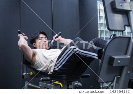 一位年輕男子在健身房進行腿部推舉訓練。 一位年輕男子在健身房進行腿部推舉訓練。 142564182