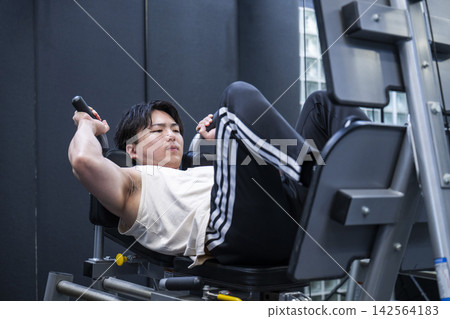 一位年輕男子在健身房進行腿部推舉訓練。 一位年輕男子在健身房進行腿部推舉訓練。 142564183