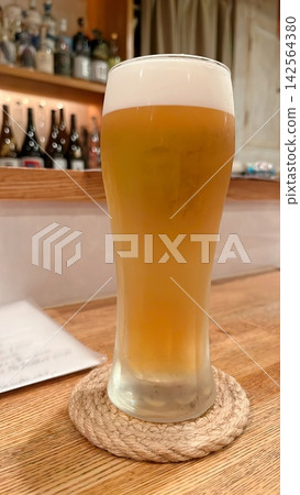 一杯泡沫豐富的啤酒放在木質櫃檯上。 一杯泡沫豐富的啤酒放在木質櫃檯上。 142564380