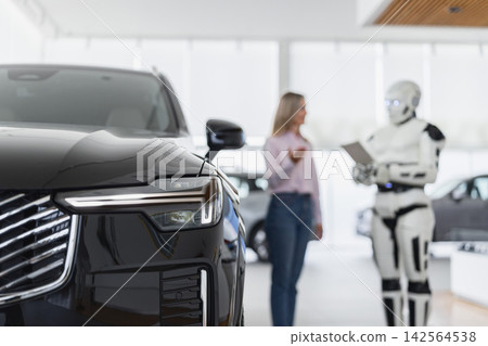 A humanoid robot interacts with a female customer in a modern car dealership showroom, discussing vehicle options A humanoid robot interacts with a female customer in a modern car dealership showroom, discussing vehicle options 142564538