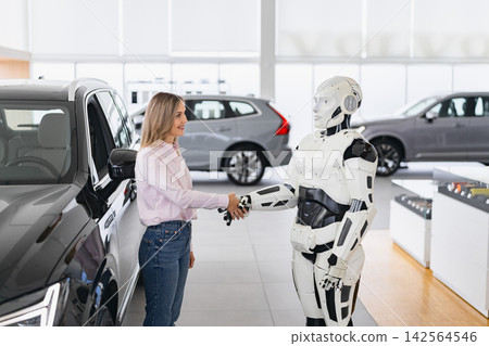 A woman shakes hands with a humanoid robot in a modern car dealership, symbolizing futuristic sales A woman shakes hands with a humanoid robot in a modern car dealership, symbolizing futuristic sales 142564546