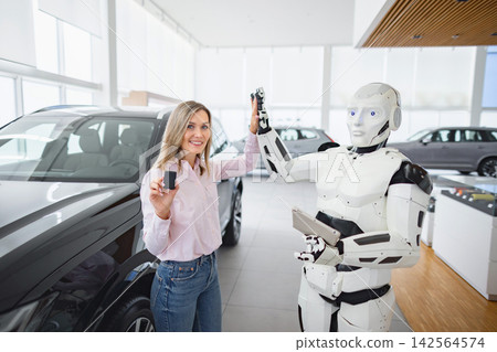 A woman receives car keys from a humanoid robot in a modern dealership showroom with vehicles in the background A woman receives car keys from a humanoid robot in a modern dealership showroom with vehicles in the background 142564574