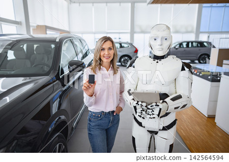 A woman holds a car key while standing next to a humanoid robot in a modern showroom with vehicles on display A woman holds a car key while standing next to a humanoid robot in a modern showroom with vehicles on display 142564594
