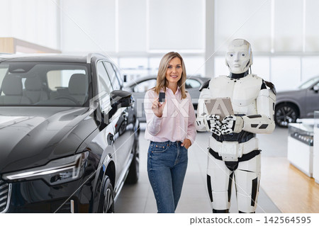 A woman holds car keys while standing next to a humanoid robot in a modern car showroom with vehicles on display A woman holds car keys while standing next to a humanoid robot in a modern car showroom with vehicles on display 142564595