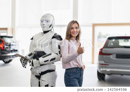 A woman gives a thumbs up next to a humanoid robot in a modern car dealership showroom A woman gives a thumbs up next to a humanoid robot in a modern car dealership showroom 142564596