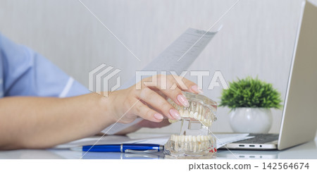 Female dentist explaining treatment plan holding transparent jaw model and medical document in clinic office. Female dentist explaining treatment plan holding transparent jaw model and medical document in clinic office. 142564674