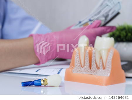 Expensive dental treatment concept showing artificial tooth implant on table and doctor holding cash dollars in background. 142564681