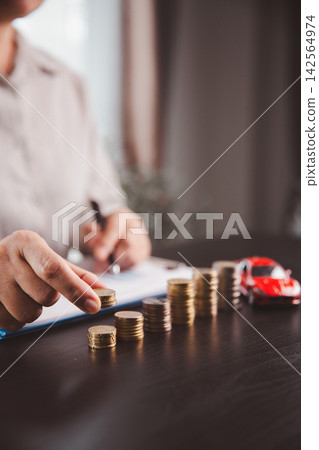 Person adds coins to ascending stacks with a red car model nearby, showing disciplined saving, auto purchase planning, down payment growth, financial progress, budgeting, and future ownership. Person adds coins to ascending stacks with a red car model nearby, showing disciplined saving, auto purchase planning, down payment growth, financial progress, budgeting, and future ownership. 142564974