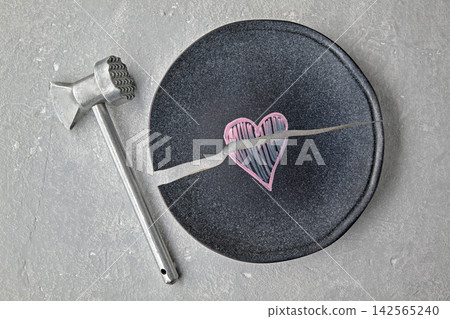 Broken ceramic plate with a broken heart drawn on it and a metal hammer on a gray concrete surface. Top view with copy space Broken ceramic plate with a broken heart drawn on it and a metal hammer on a gray concrete surface. Top view with copy space 142565240