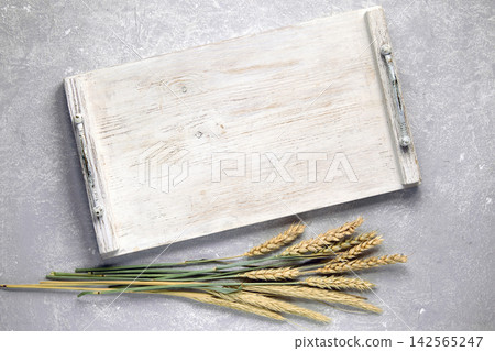 Empty white wooden tray, board with handles and dry ears of corn on gray stone table top view Empty white wooden tray, board with handles and dry ears of corn on gray stone table top view 142565247