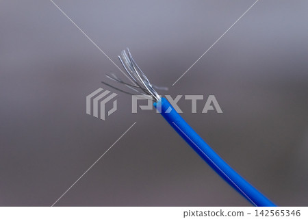 Blue electrical wire frayed metal strands stripped insulation against gray background representing cable damage repair electrical safety hazards Blue electrical wire frayed metal strands stripped insulation against gray background representing cable damage repair electrical safety hazards 142565346