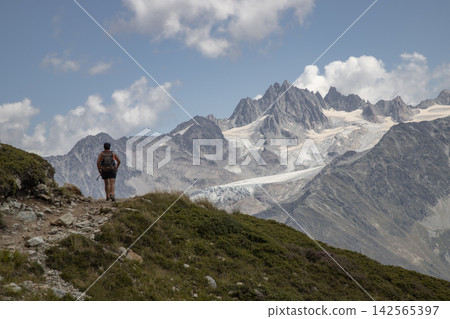 Hiker ascending mountain path with alps glaciers Hiker ascending mountain path with alps glaciers 142565397