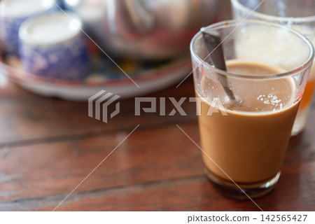Hot milk coffee served clear glass spoon wooden table creating warm casual breakfast cafe atmosphere Hot milk coffee served clear glass spoon wooden table creating warm casual breakfast cafe atmosphere 142565427