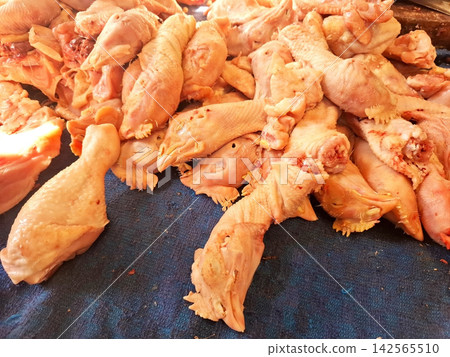 Raw skinned chicken heads piled on dark blue fabric at local butcher counter. 142565510