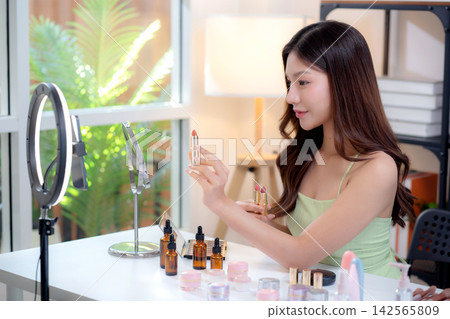 Young asian beauty influencer testing multiple lipstick shades on arm while recording makeup review. Young asian beauty influencer testing multiple lipstick shades on arm while recording makeup review. 142565809