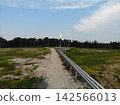 Remote pipeline facility stands in broad clearing with bright gas flare at center. Raised metal pipes follow dirt track toward dark forest, beneath expansive sky and scattered clouds. 142566013