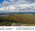 Aerial landscape of wetland plain fills frame with scattered pools, grassy earth, and distant horizon. Heavy clouds hang overhead while narrow road cuts through open land beside marsh terrain. 142566014