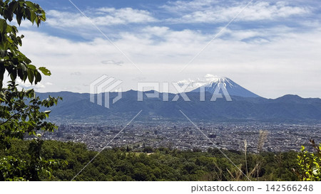 Mount Fuji, with its snow-capped peak, rises above the lush green mountains and the cityscape of Kofu. Mount Fuji, with its snow-capped peak, rises above the lush green mountains and the cityscape of Kofu. 142566248