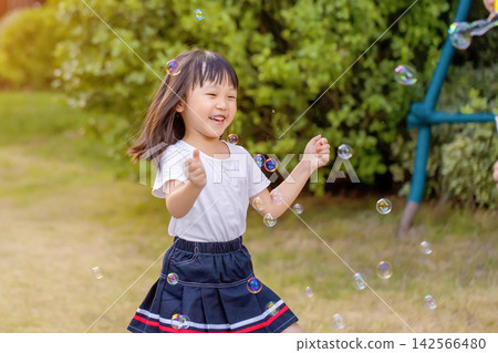 Happy Asian little girl blowing soap bubbles in sunny park, joyful childhood outdoor lifestyle Happy Asian little girl blowing soap bubbles in sunny park, joyful childhood outdoor lifestyle 142566480