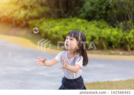 Happy Asian little girl blowing soap bubbles in sunny park, joyful childhood outdoor lifestyle 142566481