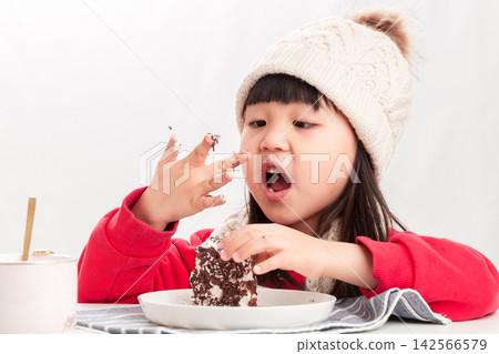 A little Asian girl dressed in winter clothes happily eats a chocolate cake, embodying the concept of dessert and birthday celebration. A little Asian girl dressed in winter clothes happily eats a chocolate cake, embodying the concept of dessert and birthday celebration. 142566579