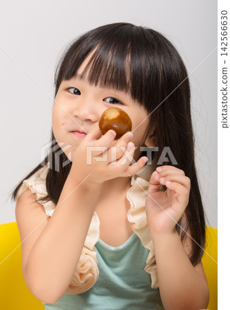 Curious little Asian girl looking at a snack in her hand before eating at table. Curious little Asian girl looking at a snack in her hand before eating at table. 142566630