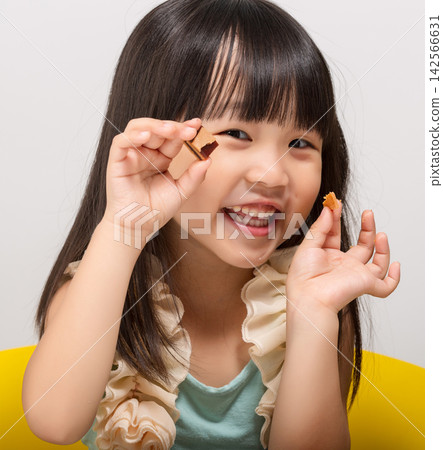 Curious little Asian girl looking at a snack in her hand before eating at table. Curious little Asian girl looking at a snack in her hand before eating at table. 142566631