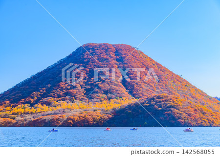 On a clear autumn morning, from the lakeshore of the Haruna Lake Memorial Park, one can see Mount Haruna, its entire mountain covered in autumn foliage, towering on the opposite shore. On a clear autumn morning, from the lakeshore of the Haruna Lake Memorial Park, one can see Mount Haruna, its entire mountain covered in autumn foliage, towering on the opposite shore. 142568055