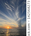 Clouds bid farewell to the setting sun as it sinks below the horizon. 142568273
