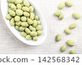 Wasabi peanuts in a white bowl, on linen. Crunchy and spicy snack made of peanut kernels, coated in savory, green wasabi-flavored shell, made of seasoned flour and corn starch, and then roasted. Photo Wasabi peanuts in a white bowl, on linen. Crunchy and spicy snack made of peanut kernels, coated in savory, green wasabi-flavored shell, made of seasoned flour and corn starch, and then roasted. Photo 142568342