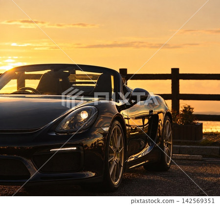 A black open-top sports car gleaming in the sunset, with beautiful body lines. A black open-top sports car gleaming in the sunset, with beautiful body lines. 142569351