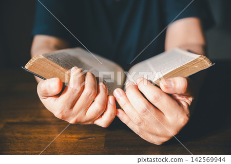 Close-up of hands turning pages of an old Bible on a wooden table, representing Christian scripture reading, faith study, devotion, worship, spiritual learning, reflection, wisdom, and religion. Close-up of hands turning pages of an old Bible on a wooden table, representing Christian scripture reading, faith study, devotion, worship, spiritual learning, reflection, wisdom, and religion. 142569944