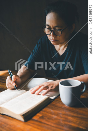 Adult person writing notes beside an open Bible and a mug on a wooden table, representing scripture study, Christian devotion, reflection, faith learning, quiet time, spiritual growth, Adult person writing notes beside an open Bible and a mug on a wooden table, representing scripture study, Christian devotion, reflection, faith learning, quiet time, spiritual growth, 142569972