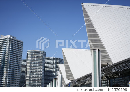 高聳入雲的公寓大樓在藍天和現代城市景觀的背景下熠熠生輝。 高聳入雲的公寓大樓在藍天和現代城市景觀的背景下熠熠生輝。 142570398