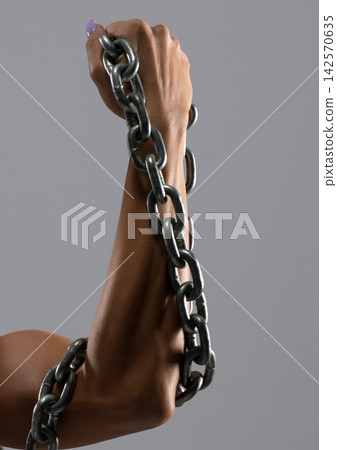 Strong arm holding a metal chain, symbolizing struggle and resilience in a creative setting Strong arm holding a metal chain, symbolizing struggle and resilience in a creative setting 142570635
