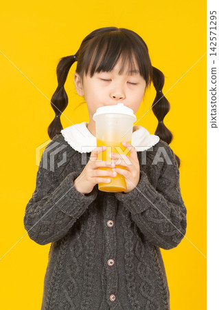 Cute Asian little girl holding a glass of orange juice on yellow studio background Cute Asian little girl holding a glass of orange juice on yellow studio background 142571295