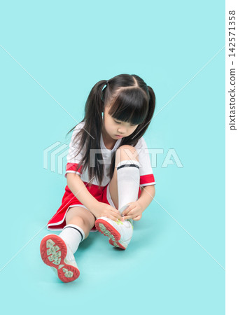 Cute young girl in red and white sportswear sitting on the floor and tying her running shoes. Cute young girl in red and white sportswear sitting on the floor and tying her running shoes. 142571358