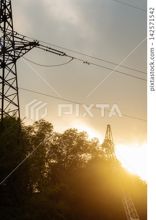High voltage power pylon and crane silhouette against golden sunset sky outdoor High voltage power pylon and crane silhouette against golden sunset sky outdoor 142571542