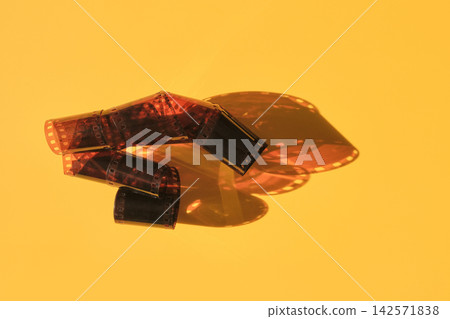 Film negatives unrolling on yellow background, creating shadows and vintage aesthetic Film negatives unrolling on yellow background, creating shadows and vintage aesthetic 142571838
