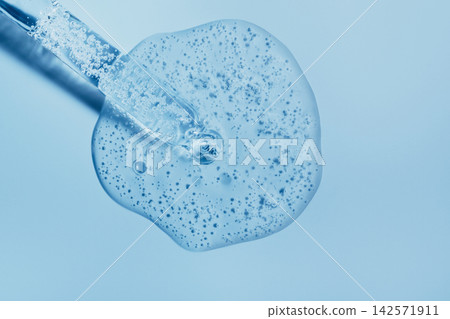 Pipette applying gel serum with bubbles for skincare treatment on blue surface Pipette applying gel serum with bubbles for skincare treatment on blue surface 142571911