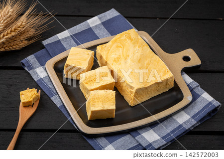 Crispy dalgona honeycomb candy cubes with honey on a black square plate Crispy dalgona honeycomb candy cubes with honey on a black square plate 142572003