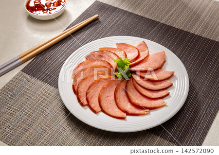 dipping sliced Chinese pine nut pork sausage into spicy chili oil, savory cold appetizer preparation dipping sliced Chinese pine nut pork sausage into spicy chili oil, savory cold appetizer preparation 142572090
