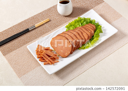 dipping sliced Chinese pine nut pork sausage into spicy chili oil, savory cold appetizer preparation 142572091