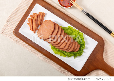 dipping sliced Chinese pine nut pork sausage into spicy chili oil, savory cold appetizer preparation dipping sliced Chinese pine nut pork sausage into spicy chili oil, savory cold appetizer preparation 142572092