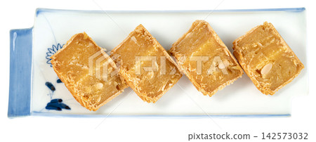 Four pieces of traditional Asian mung bean cake with melon seeds served on a decorative white and blue ceramic plate Isolated. Professional top view for food packaging. Four pieces of traditional Asian mung bean cake with melon seeds served on a decorative white and blue ceramic plate Isolated. Professional top view for food packaging. 142573032