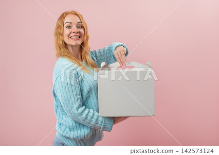 Cheerful red haired woman with an excited expression looking at the viewer, holding and opening a white blank cardboard box, revealing its contents or preparing for delivery Cheerful red haired woman with an excited expression looking at the viewer, holding and opening a white blank cardboard box, revealing its contents or preparing for delivery 142573124