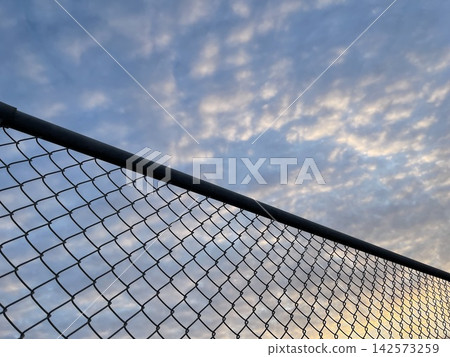 The silhouette of the wire mesh fence against the evening sky The silhouette of the wire mesh fence against the evening sky 142573259